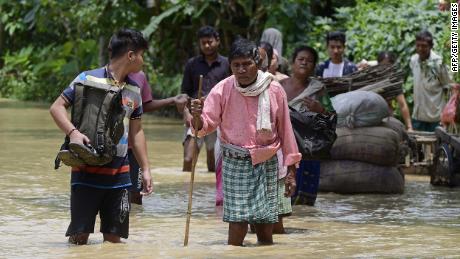 Pessoas caminham nas águas da enchente no distrito de Nagoon, no estado indiano de Assam, em 18 de maio.