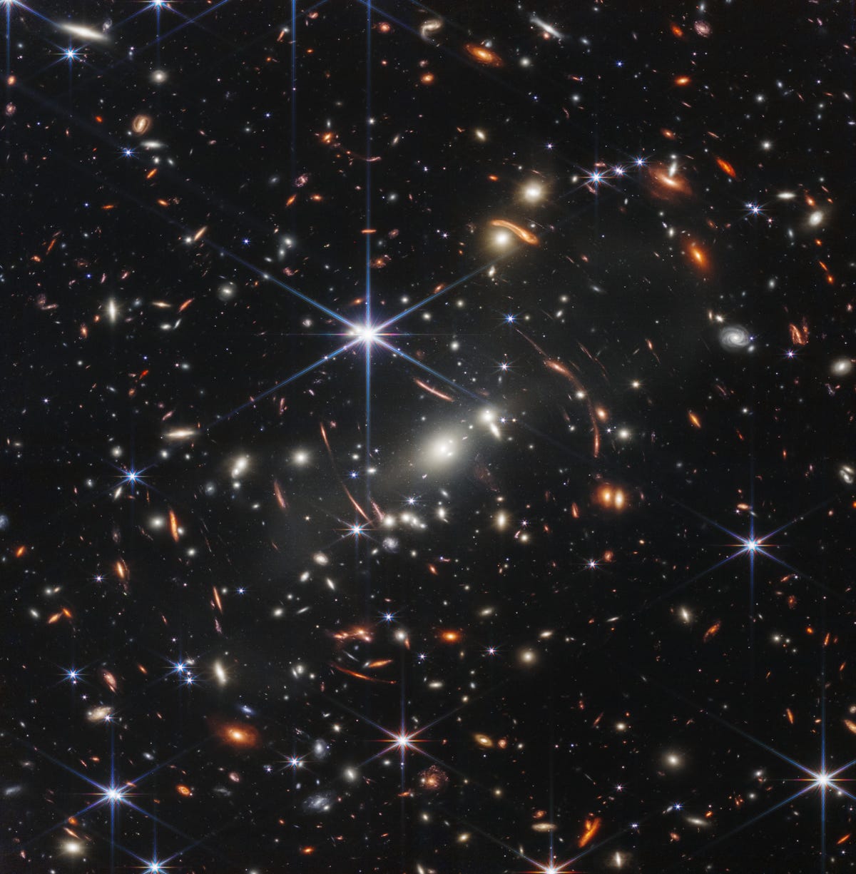Um campo de milhares de galáxias contra a escuridão do espaço com uma grande estrela azul central de seis pontas.