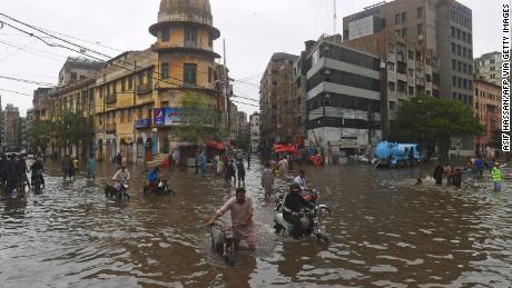 Pessoas caminham em uma rua inundada após fortes chuvas de monção em Karachi em 25 de julho.