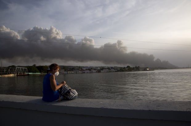 Um morador senta-se no paredão de Malecón enquanto a fumaça do incêndio sobe ao fundo.