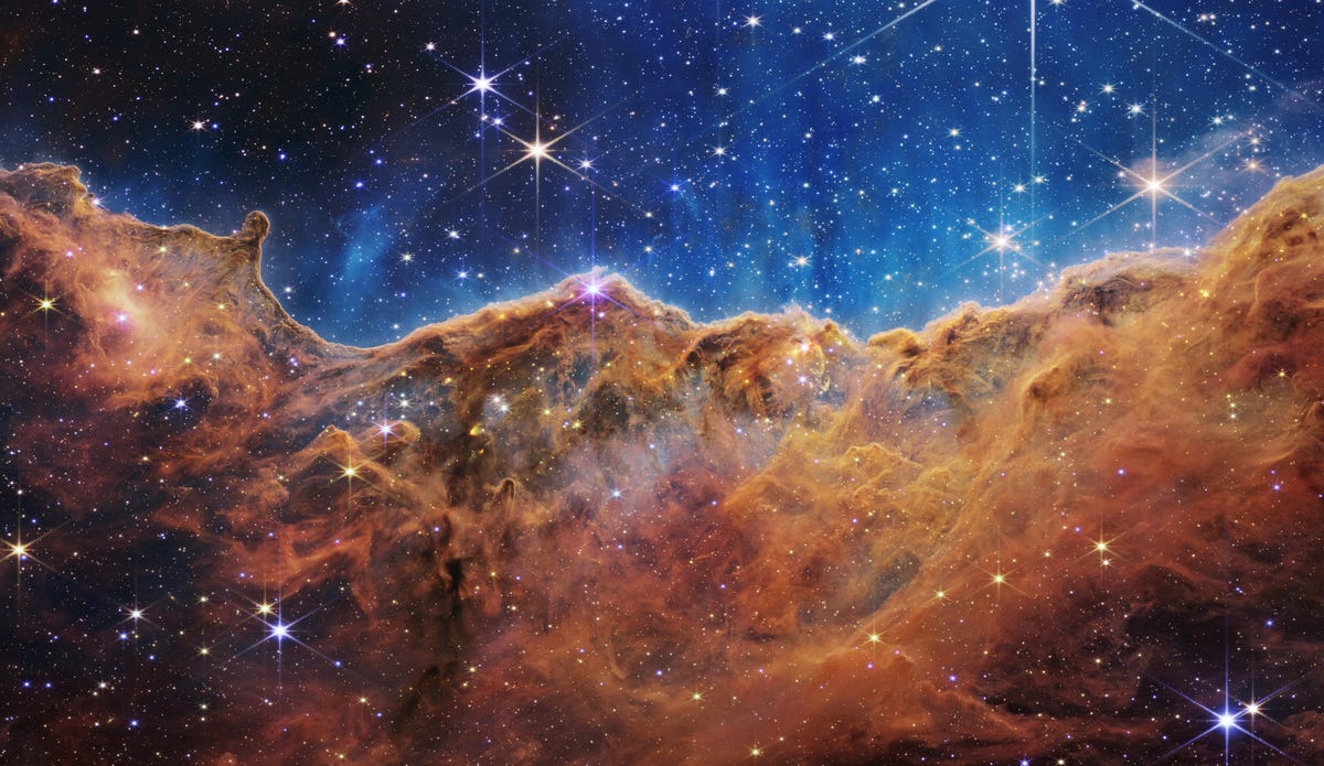 A Nebulosa Carina: Estrelas brilham contra um fundo índigo acima das nuvens de gás de bronze enferrujado