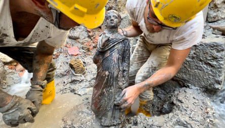 Dois arqueólogos seguram uma estátua de um menino.