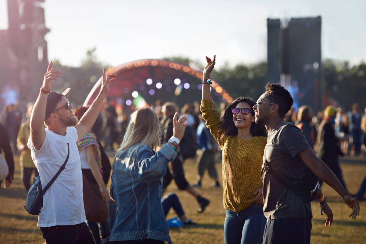 Grupo de amigos dançando no meio da multidão enquanto caminham no palco em um festival de música.