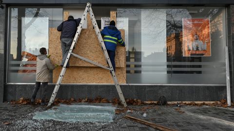 Homens inserem pranchas de madeira na janela de um banco próximo ao prédio da Administração Estatal de Kherson após um ataque com foguete na cidade de Kherson na quarta-feira.
